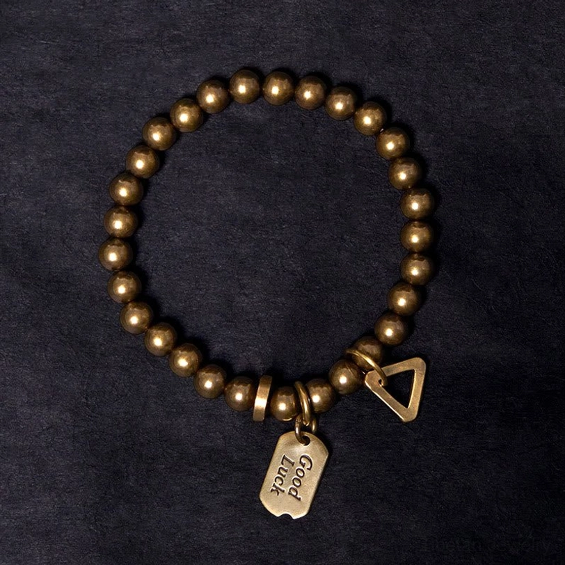 Antique bronze beaded bracelet overhead shot on dark fabric background displaying smooth round beads and dual charm ornaments