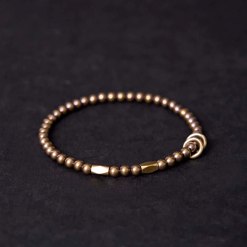Tibetan brass couple bracelet with oval metal clasp and uniform round beads on dark fabric background