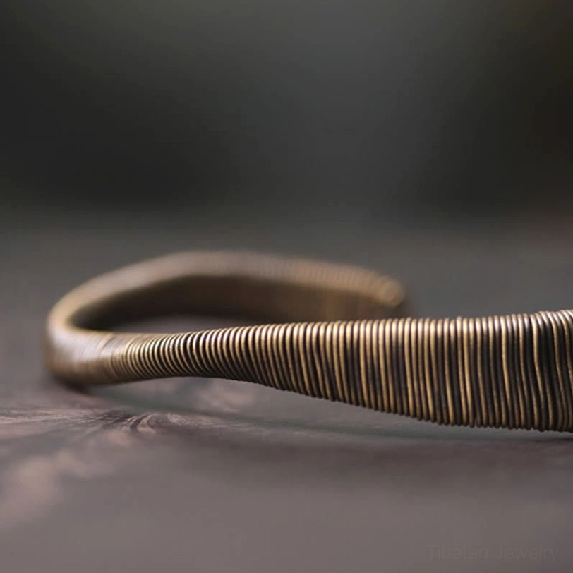 Adult wrist wearing dark bronze tone Tibetan cuff bracelet with slim wire wrap, indoor lifestyle perspective