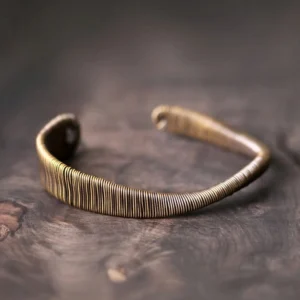 Tibetan wrapped brass adjustable cuff bracelet with tightly coiled wire texture and open design, viewed from high side angle on dark wooden surface