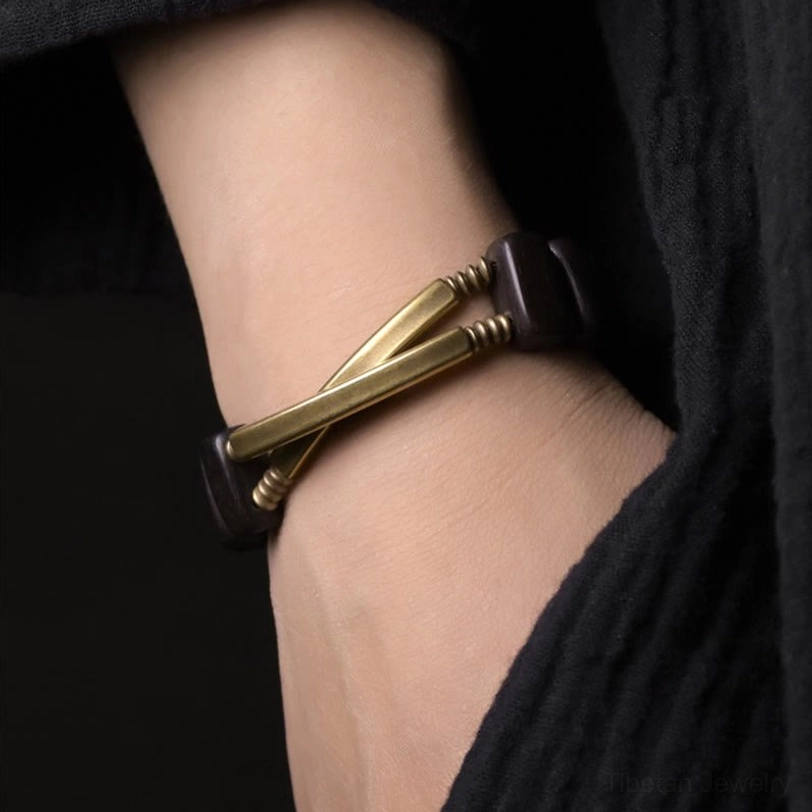 Cross-style double layer ebony brass bracelet worn on wrist, side angle close-up photo featuring overlapped gold brass bars with single ebony bead detail against black fabric