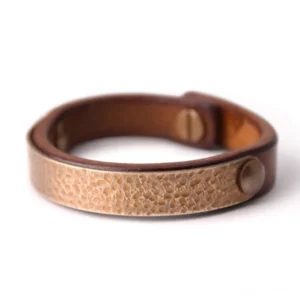 Tibetan prosperity bracelet featuring light gold hammered brass panel with round rivet closure on vintage brown leather, overhead front view