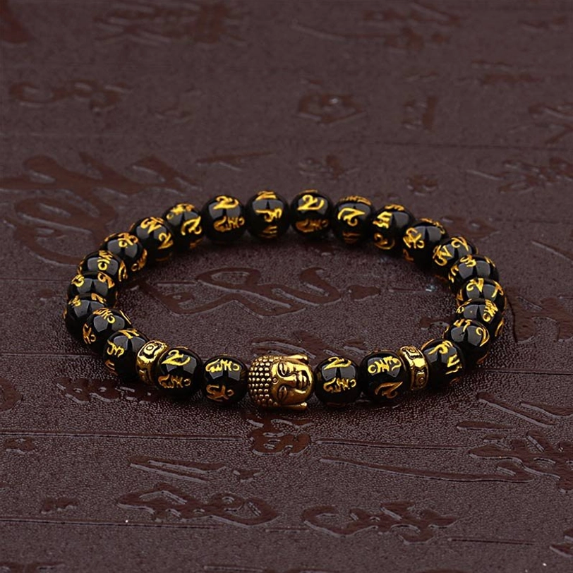 Six True Words Tibetan Buddhist bracelet with gold-engraved beads and gold Buddha charm displayed on dark wooden table