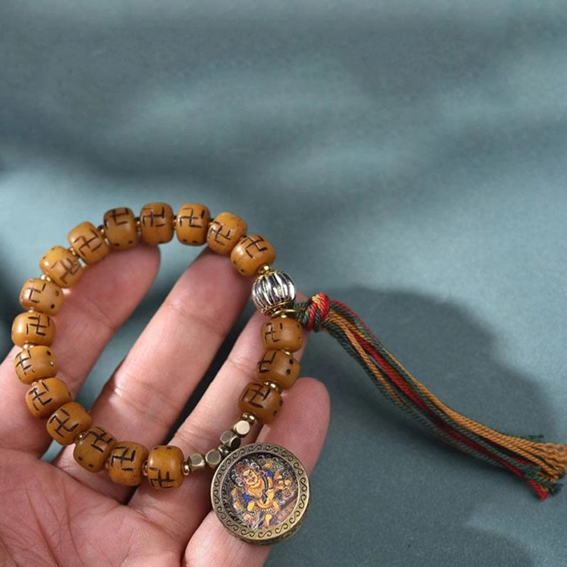Close-up hand-held photo of Tibetan camel bone Buddha bracelet with carved beads, bronze Buddha medallion, silver accents, and braided tassel