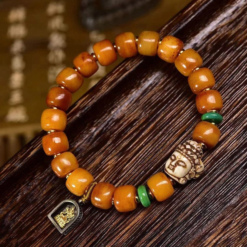 Handmade Tibetan luck bracelet featuring aged camel bone barrel beads, green spacers, and buddha head charm with stamped metal pendant on wooden board