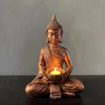 Tibetan Buddha tealight candleholder with lit candle on minimalist table setting, bronze weathered finish with ornate robe details