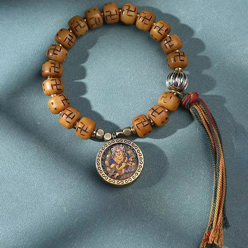 Flat lay photography of Tibetan Buddha charm bracelet showing tan bone beads, round bronze Buddha plaque, silver metal beads, and red-brown tassel