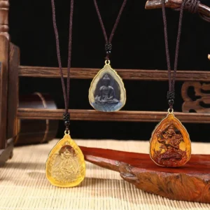 Three Tibetan Buddha crystal pendants in different colors displayed on wooden stand with bamboo mat background
