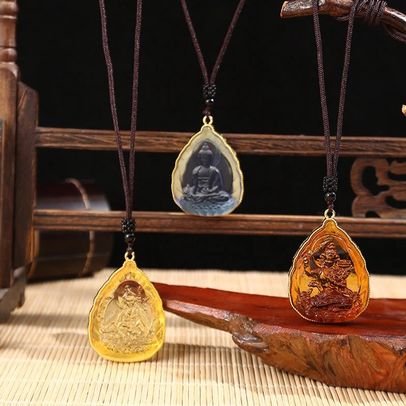 Three Tibetan Buddha crystal pendants in different colors displayed on wooden stand with bamboo mat background
