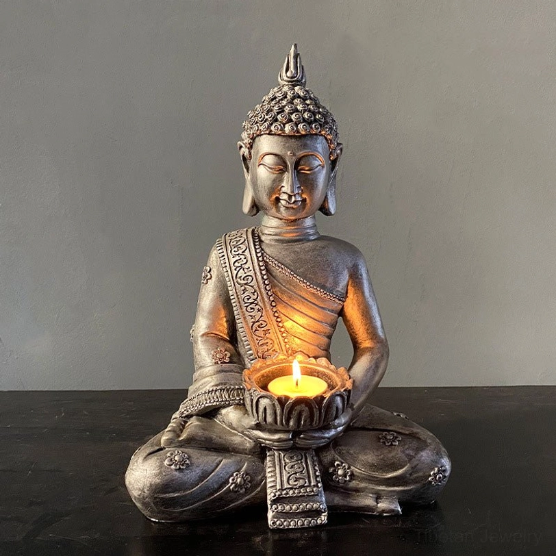 Dark-toned Tibetan Buddha tealight holder with aged grey finish, lit candle on minimalist table, detailed robe patterns