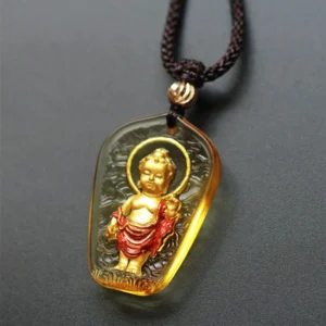 Tibetan Baby Buddha Liuli crystal pendant necklace with amber translucent stone, gilded Buddha figure with red painted robe and halo, front view on dark background