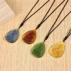 Four color options of Tibetan Buddha Liuli crystal pendants with gold-plated rims and black beaded cords on bamboo mat