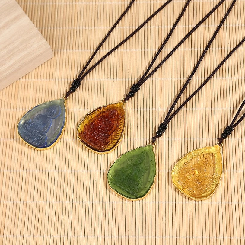 Four color options of Tibetan Buddha Liuli crystal pendants with gold-plated rims and black beaded cords on bamboo mat
