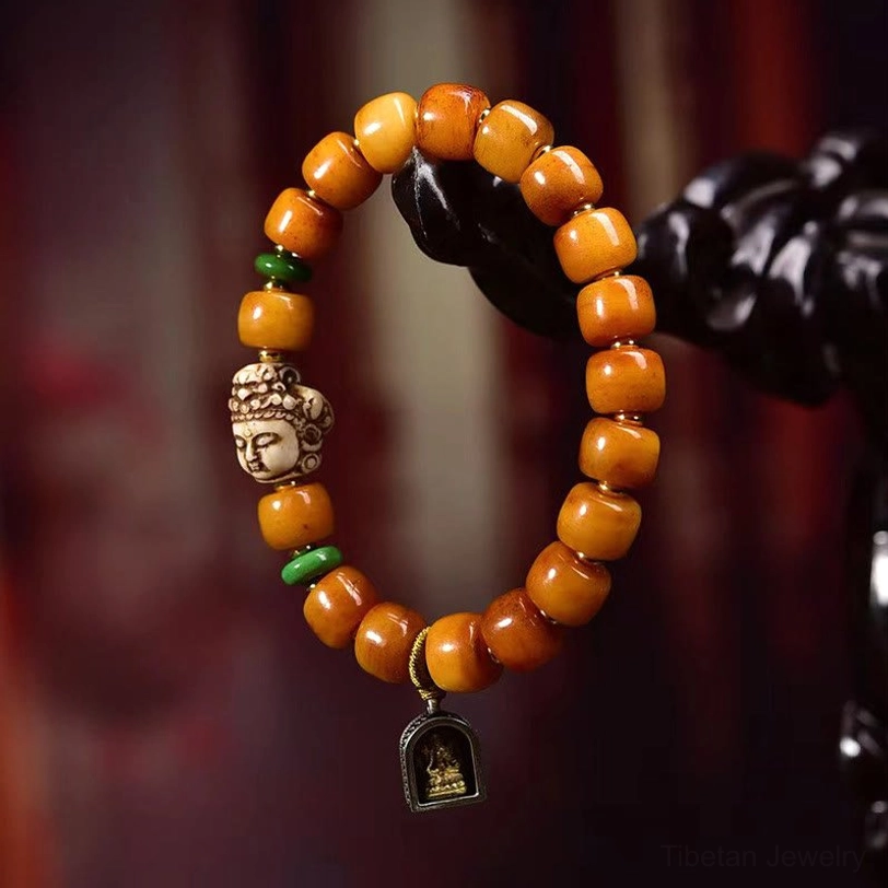 Sacred Buddha head protection bracelet with tan camel bone beads, green spacers, and small black metal charm hanging on display stand