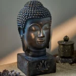 Tibetan Buddha head statue with aged bronze finish and lotus relief base, displayed on linen meditation table with three-quarter front view