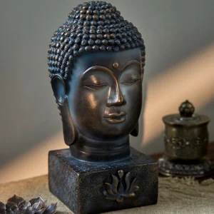 Tibetan Buddha head statue with aged bronze finish and lotus relief base, displayed on linen meditation table with three-quarter front view