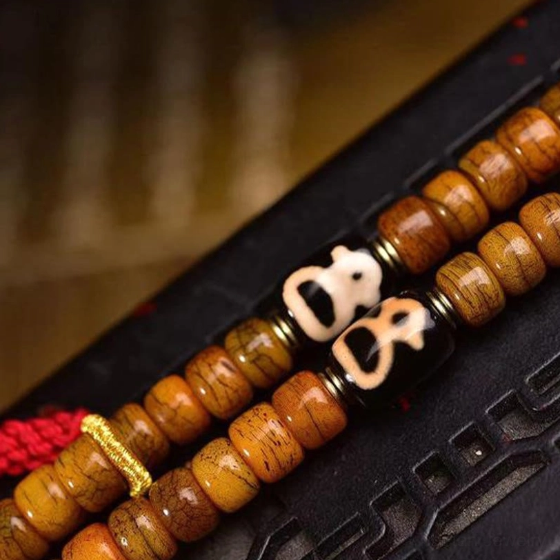 Close-up detail of camel bone prayer beads with Dzi bead and carved metal shrine pendant on wooden surface