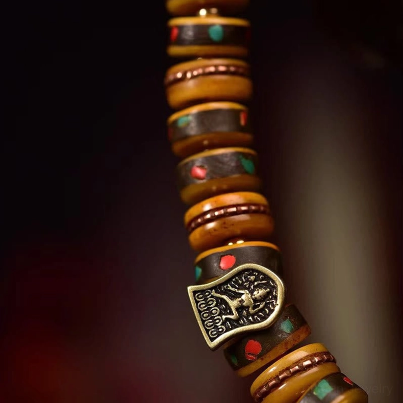 Close-up macro detail of Tibetan camel bone beads showing carved disc pattern, red-green inlay segments and bronze Buddha charm