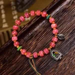 Handcrafted Tibetan camel bone bracelet with red agate beads and silver copper charms on wood background