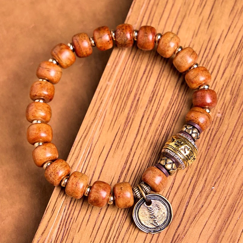 Side angle of Tibetan bone bead bracelet with rounded barrel beads and decorative metal OM charm on wooden board