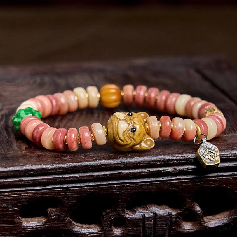 Tibetan pug luck protection bracelet displayed on carved dark wooden tray with pink and tan bone beads and enamel charm