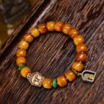 Tibetan camel bone Buddha protection bracelet with carved buddha bead, green spacer beads, and metal pendant on dark wood surface - flat lay view