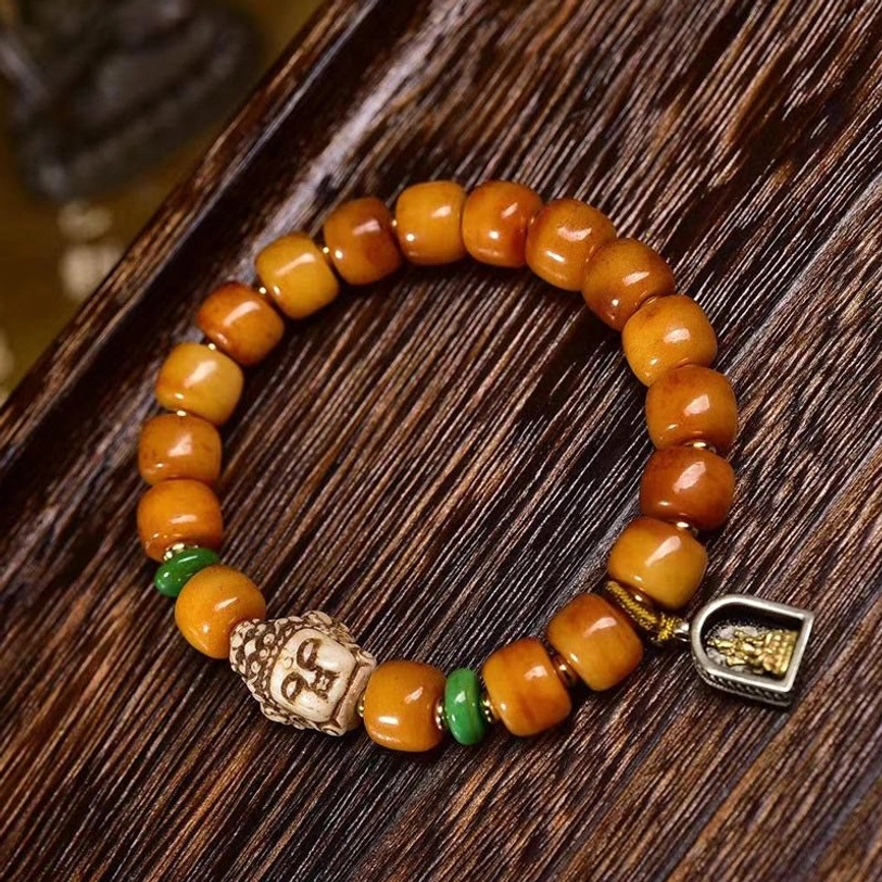 Tibetan camel bone Buddha protection bracelet with carved buddha bead, green spacer beads, and metal pendant on dark wood surface - flat lay view