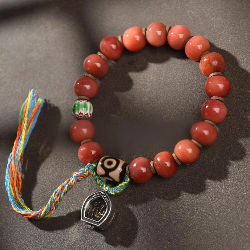 Tibetan camel bone bracelet with nine-eye dzi bead, red agate beads, multicolor silk tassel, and copper charm pendant in overhead flat lay view