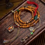 Tibetan 108 camel bone mala beads flat lay with Dzi beads, ritual charms, and red silk tassel on dark wooden surface