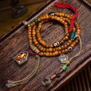 Tibetan 108 camel bone mala beads flat lay with Dzi beads, ritual charms, and red silk tassel on dark wooden surface