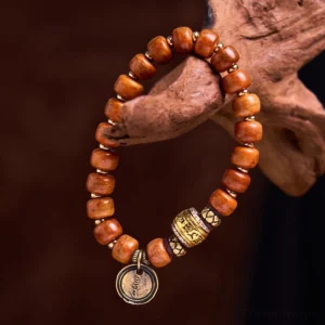 Tibetan camel bone OM bracelet with reddish barrel beads and metal Sanskrit charm on warm wooden background - close-up detail view