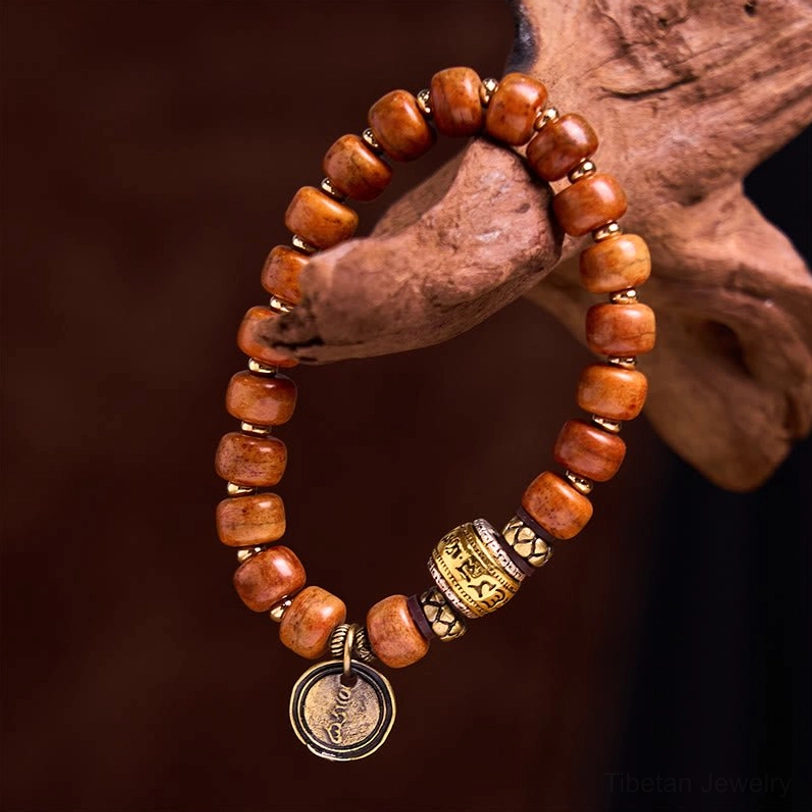 Tibetan camel bone OM bracelet with reddish barrel beads and metal Sanskrit charm on warm wooden background - close-up detail view