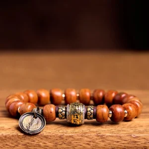 Handmade Tibetan prayer bead bracelet flat lay showing barrel bone beads, engraved metal beads and round OM pendant on wooden table