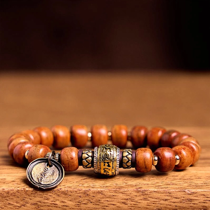 Handmade Tibetan prayer bead bracelet flat lay showing barrel bone beads, engraved metal beads and round OM pendant on wooden table