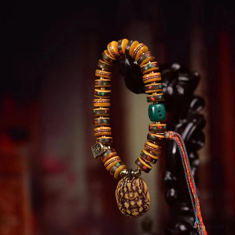 Tibetan camel bone dice bracelet front display on red background showing carved pendant, inlaid stones, and protective tassel detail