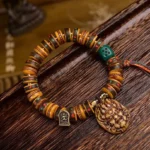 Tibetan camel bone dice bracelet with carved deity pendant and bronze charm on wooden tray, overhead view showing protective tassel and natural bone beads