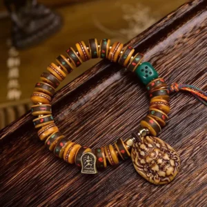 Tibetan camel bone dice bracelet with carved deity pendant and bronze charm on wooden tray, overhead view showing protective tassel and natural bone beads