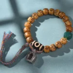 Tibetan camel bone swastika bracelet with black and white dzi bead and silver ga'u charm on teal background - overhead flat lay view