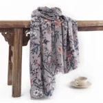 Tibetan camellia floral scarf with vintage blooming flower print, dusk grey retro wrap draped over vintage wooden table with coffee set styling