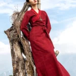 Tibetan wrap maxi dress with auspicious cloud pattern in burgundy, full-length outdoor model shot showing cross V-neck and waist tie detail