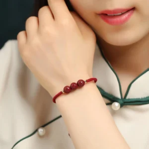 Tibetan cinnabar mantra bracelet worn on wrist with red cord and engraved beads, close-up side view on cheongsam fabric