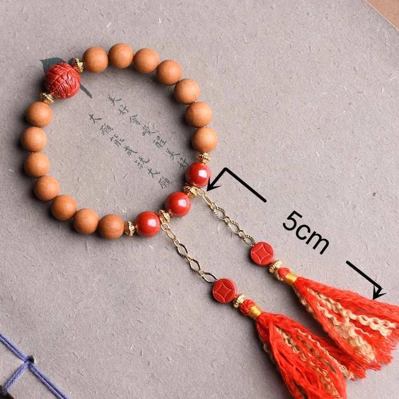 Tibetan peach wood cinnabar bracelet with 5cm scale marker showing size, dual red silk tassels with gold accents on calligraphy paper