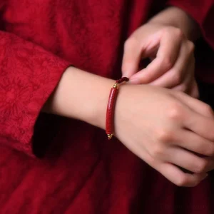 Sacred mantra blessing bracelet worn on wrist, showing deep red braided cord and engraved cinnabar stone