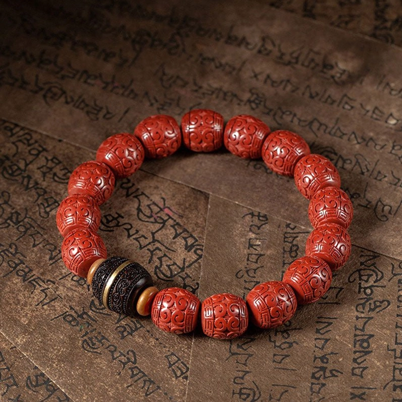 Handcrafted cinnabar ebony bracelet displayed overhead on Buddhist text background, showing round carved red beads with black ebony accents