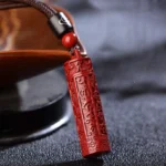 Tibetan cinnabar mantra necklace close-up showing red carved pendant with black cord and accent beads on wooden display holder