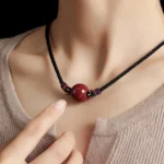 Tibetan cinnabar bead necklace worn close-up on neck showing round red pendant with black woven cord and colorful braided knots