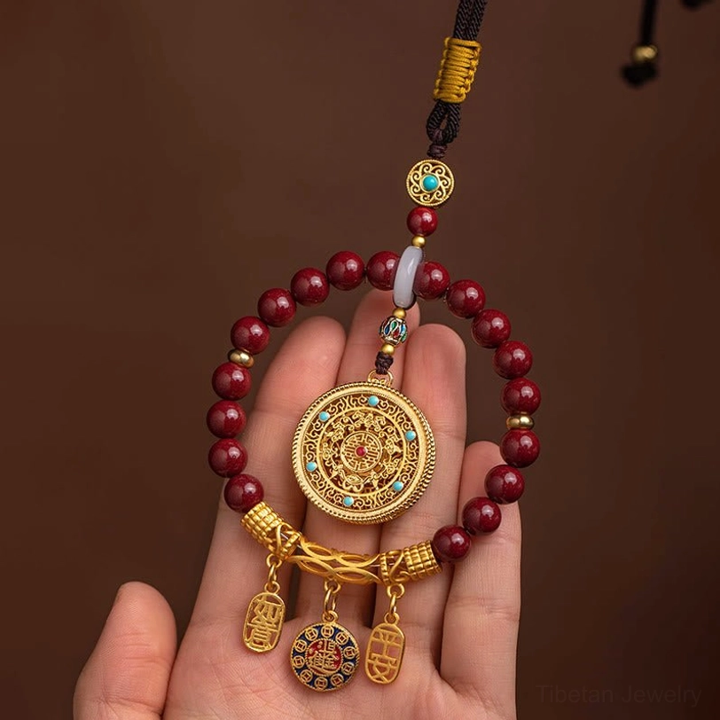 Hand-held close-up of tibetan cinnabar ruyi peace ornament showing maroon beads resting on palm with engraved gold pendant detail