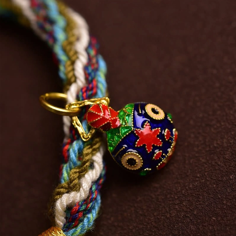 Close-up detail of Tibetan cloisonné enamel charm with gold clasp attached to braided fortune bracelet cord