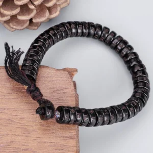 Tibetan Om Mani Padme Hum coconut shell mantra bracelet with engraved beads and fabric tassel, displayed on wooden surface with natural lighting
