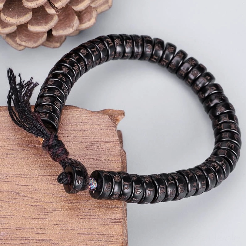 Tibetan Om Mani Padme Hum coconut shell mantra bracelet with engraved beads and fabric tassel, displayed on wooden surface with natural lighting